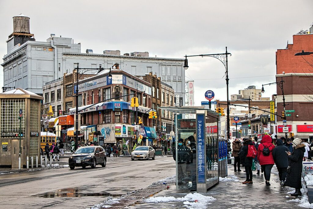 A busy street in the Bronx, New York, lined with shopfronts and apartment buildings.