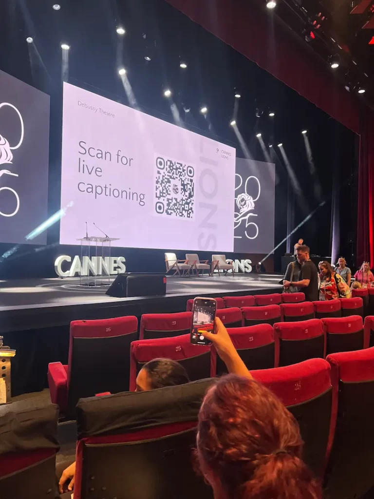 An audience member holds up their phone to scan a QR code projected on the stage screen to access live captions.