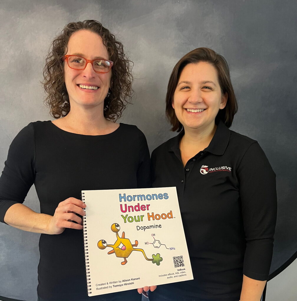 The Deaf interpreter and an ICS team member in a branded polo stand together against the studio backdrop, holding up the printed Dopamine book.