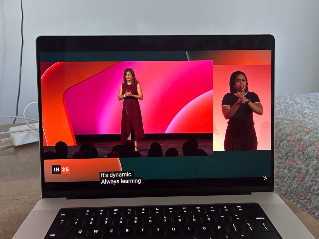 A remote attendee's laptop showing the INBOUND livestream: the speaker on stage in the main frame and the ASL interpreter in a dedicated panel to the right, with open captions along the bottom.
