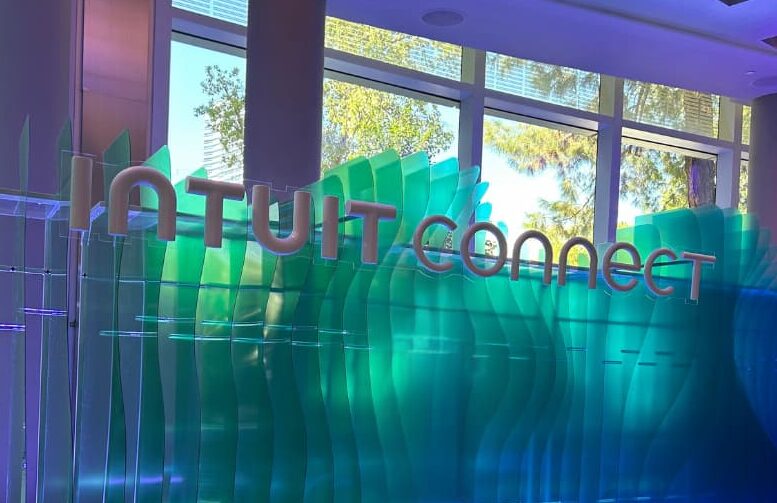 The Intuit Connect entrance installation: a wall of translucent green and blue sculpted panels carrying the words 'Intuit Connect' in raised lettering, with daylight and trees visible through the windows behind it.