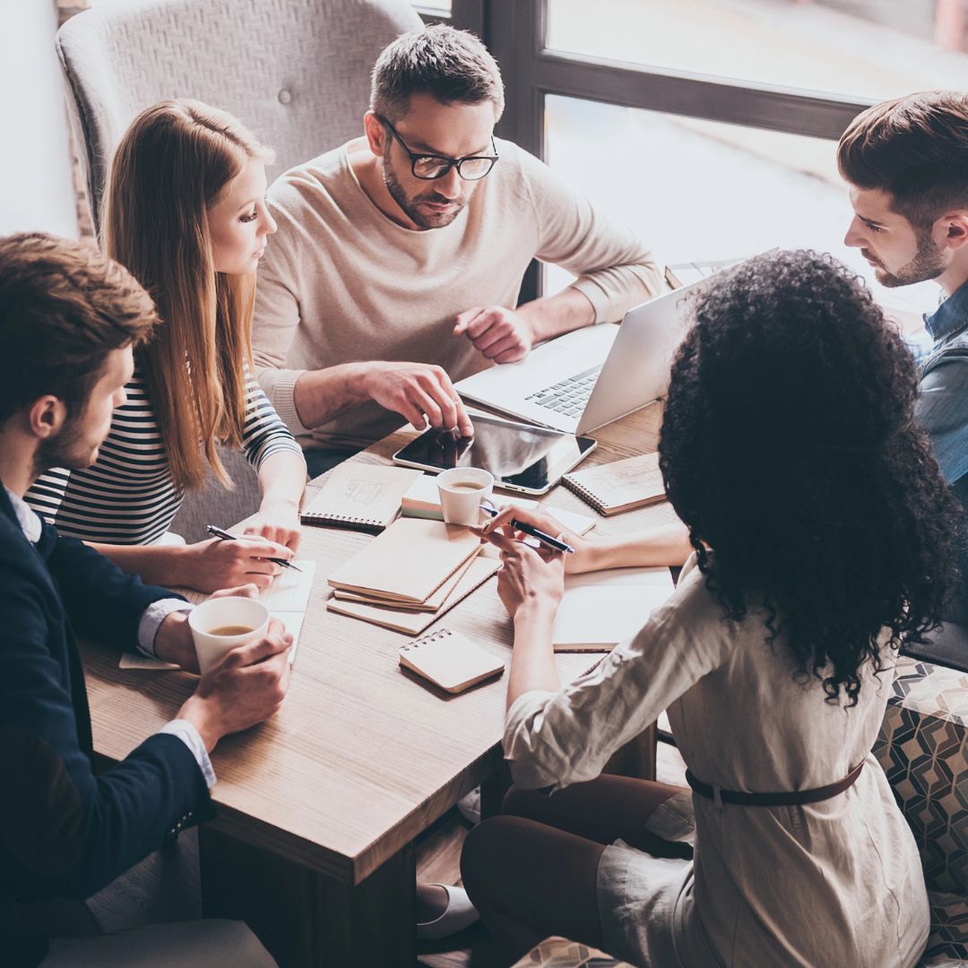 Five colleagues gather around a table for an in-person meeting.