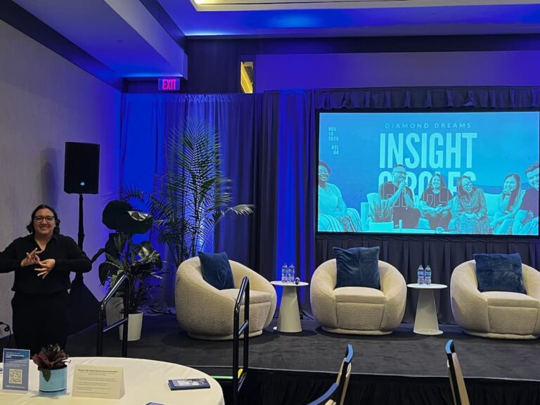 Conference room with a small stage, cozy chairs, and a screen displaying “Insight Circles.” A sign language interpreter stands to stage left.