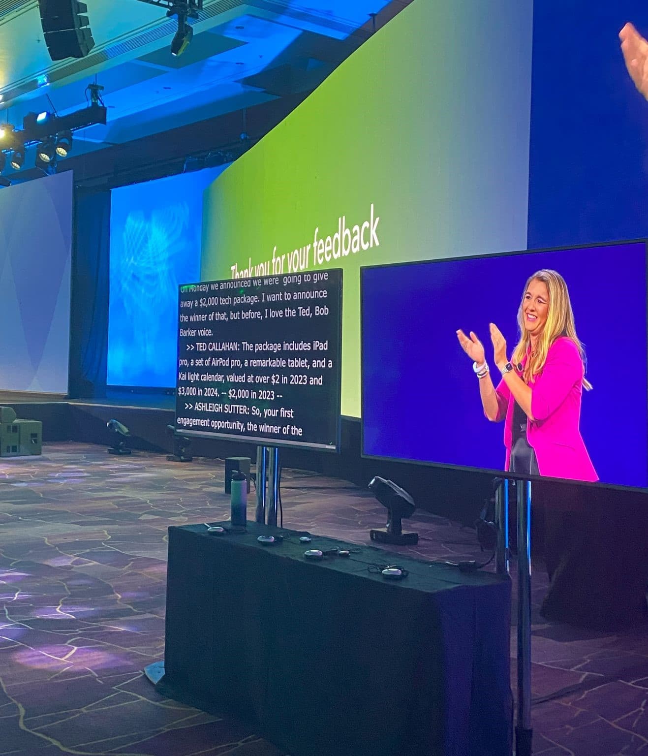A conference stage screen shows live captions beside a video feed of a speaker applauding