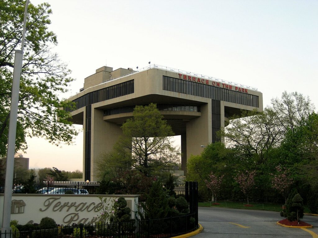 Terrace On The Park raised above Flushing Meadows-Corona Park on its concrete piers, the Manhattan skyline behind it.
