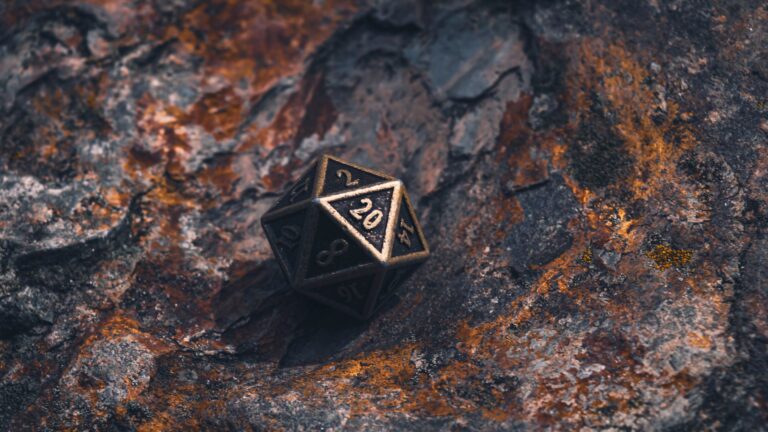 A metal d20 die on a textured, multicolored rock surface.