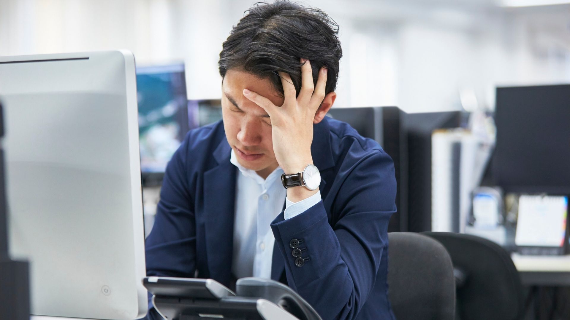 A man sits at his desk, his head in his hand, conveying the quiet exhaustion and isolation that can accompany communication challenges at work.