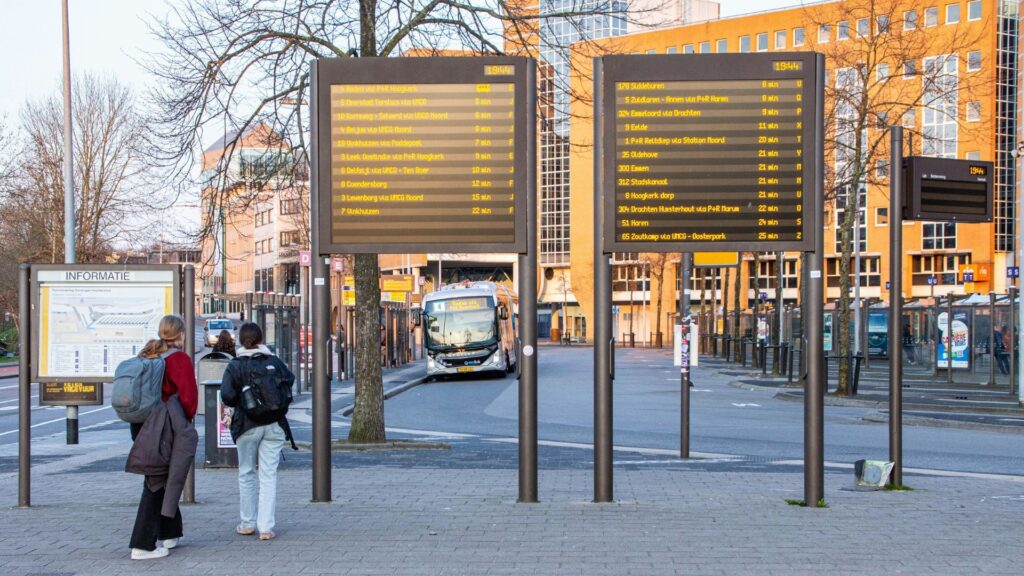 From Airports to Attractions: Where Communication Breaks Down for Deaf Travellers 1 Bus terminal with electronic schedule boards and a parked bus in an urban area.